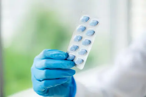 Ręka w niebieskiej rękawiczce trzyma opakowanie z niebieskimi tabletkami, które mogą pomóc w problemach z potencją.