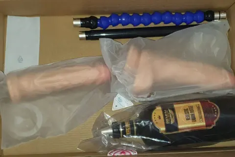 W pudełku leży maszyna erotyczna: dwa realistyczne falusy, butelka imitująca alkohol i dwa giętkie wężyki.