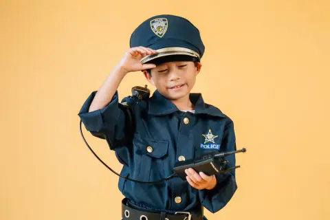 Chłopiec w stroju policjantki, z czapką na głowie i krótkofalówką w ręku, gotowy do akcji.