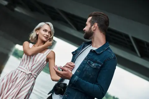 Kobieta w sukience w paski i mężczyzna z aparatem rozmawiają. Może to być wskazówka, co zrobić, by facet cię szanował: bądź sobą i rozwijaj swoje pasje.