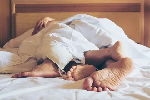 Stopy w pościeli, dłonie splatające się pod kołdrą. Chwila intymności, sensualny sex.