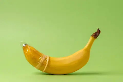 Banan w prezerwatywie, symbolizujący penis 23 cm, na zielonym tle.